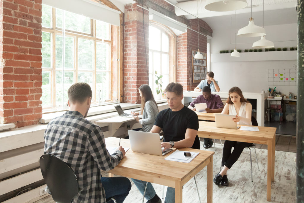 Young casually dressed employees at work in coworking office. Corporate team working on laptops and taking notes in shared room, brainstorming about new project, teamwork and collaboration concept.