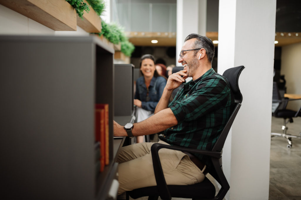 Employees talk amongst eacn other as they work on their computers in their modernized workplace/office space. 