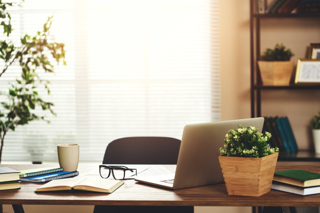 Home office desk with computer, glasses against a bright window